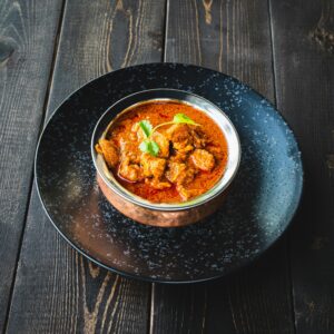 Mouthwatering spicy chicken curry garnished with cilantro, served on a rustic wooden table.