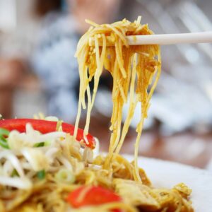 Close-up of a flavorful noodle dish with chopsticks lifting noodles, perfect for food photography.