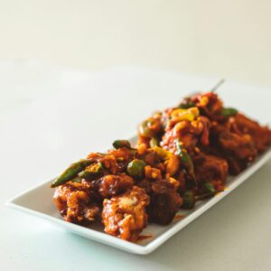 Close-up of spicy chicken Manchurian curry garnished with green peppers on a white dish.